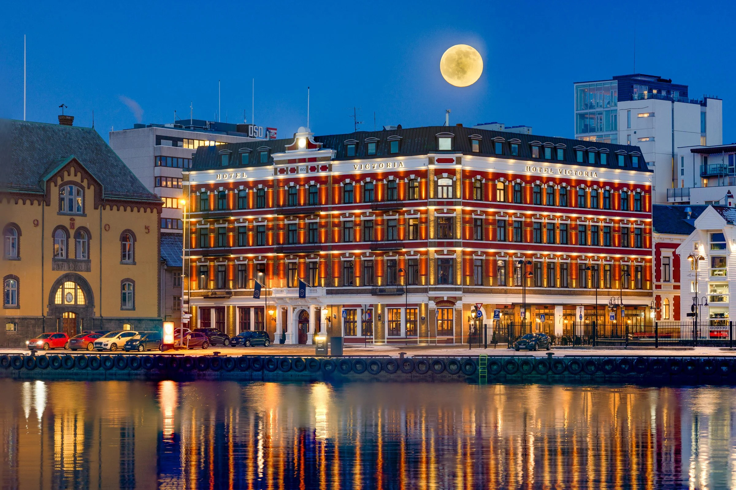 Hotel Victoria i Stavanger opplyst om kvelden, med speilinger i vannet